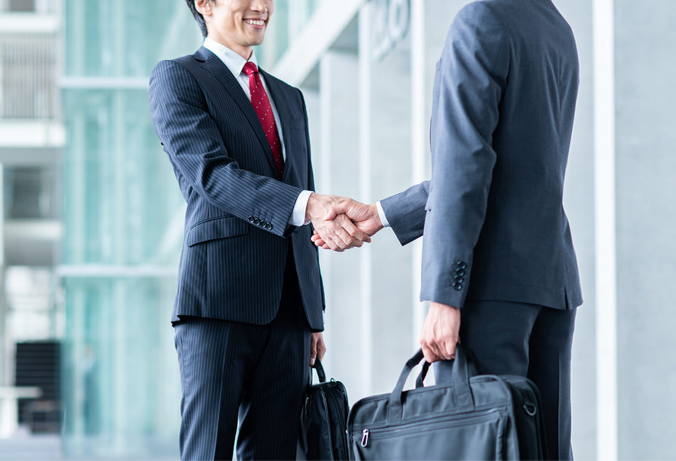 男性会社員ふたりが会社外で握手している写真